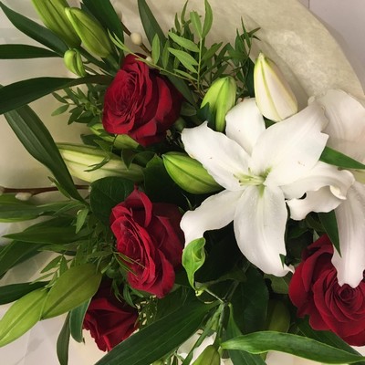 Hand-tied bouquet with red Freedom roses, white lilies, willow accents and foliage, wrapped in luxury cellophane and gift bag.