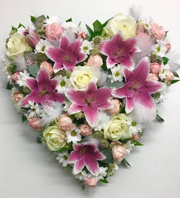 Heart-shaped funeral tribute in pink and white with luxury flowers, white feathers, glitter, and diamantes.