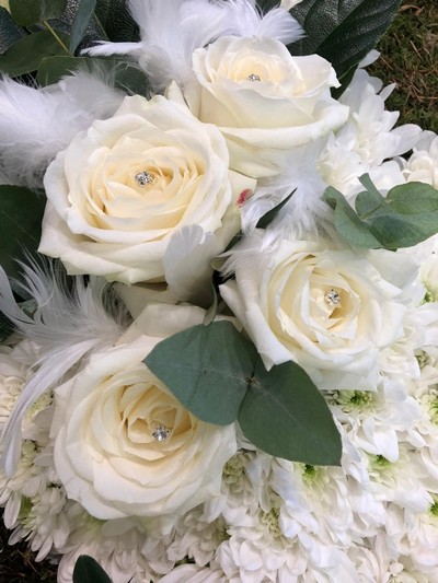 Dove-shaped funeral tribute made with white chrysanthemum on a moss base, featuring a white rose focal, feather and diamanté details, measuring approximately 36 inches high by 24 inches wide.