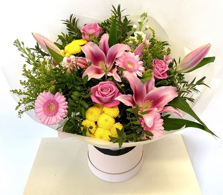Pink and yellow seasonal florist’s choice hatbox arrangement with mixed florals and greenery.