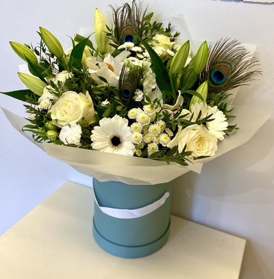 White seasonal florist’s choice hatbox arrangement with greenery and peacock feathers.