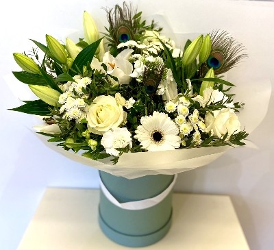 White seasonal florist’s choice hatbox arrangement with greenery and peacock feathers.