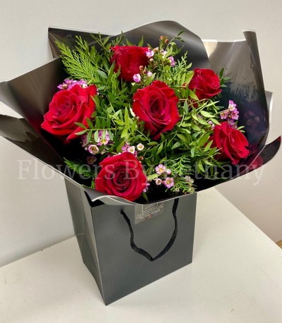Bouquet featuring 6 luxury red roses with a filler florals, accented with diamanté in the roses, complemented by foliage, wrapped in luxury cellophane and matching gift bag, hand-tied in water.