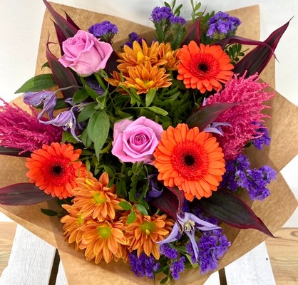 Summer Sunset bouquet with orange roses, purple clematis and pink astilbe, hand-tied in luxury gift wrap.