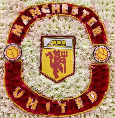 Manchester United badge-shaped funeral tribute made with white and yellow chrysanthemum, red carnations, and pipe cleaner with laminated detailing on a 24