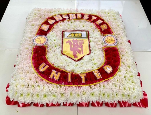 Manchester United badge-shaped funeral tribute made with white and yellow chrysanthemum, red carnations, and pipe cleaner with laminated detailing on a 24