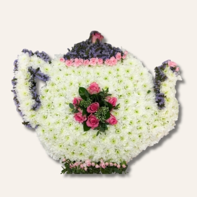 Teapot-shaped funeral tribute made with white chrysanthemum base and pink and lilac floral accents, measuring approximately 58cm x 61cm.