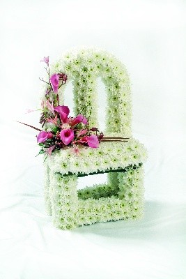 3D vacant chair-shaped funeral tribute made with white chrysanthemum and a soft pink floral focal on the seat, measuring approximately 57cm high, 28cm wide, and 21cm deep.