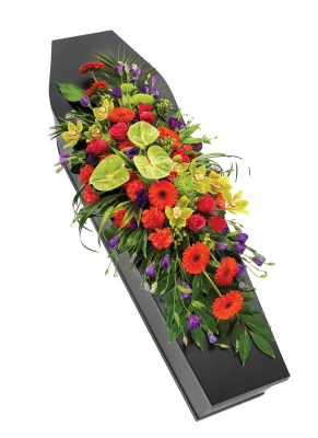 Colourful casket spray with tropical and seasonal blooms in orange, green, and purple, set on lush foliage.
