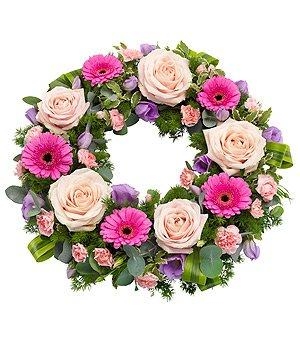 Funeral wreath with pink and lilac seasonal flowers, accented with lush green foliage.