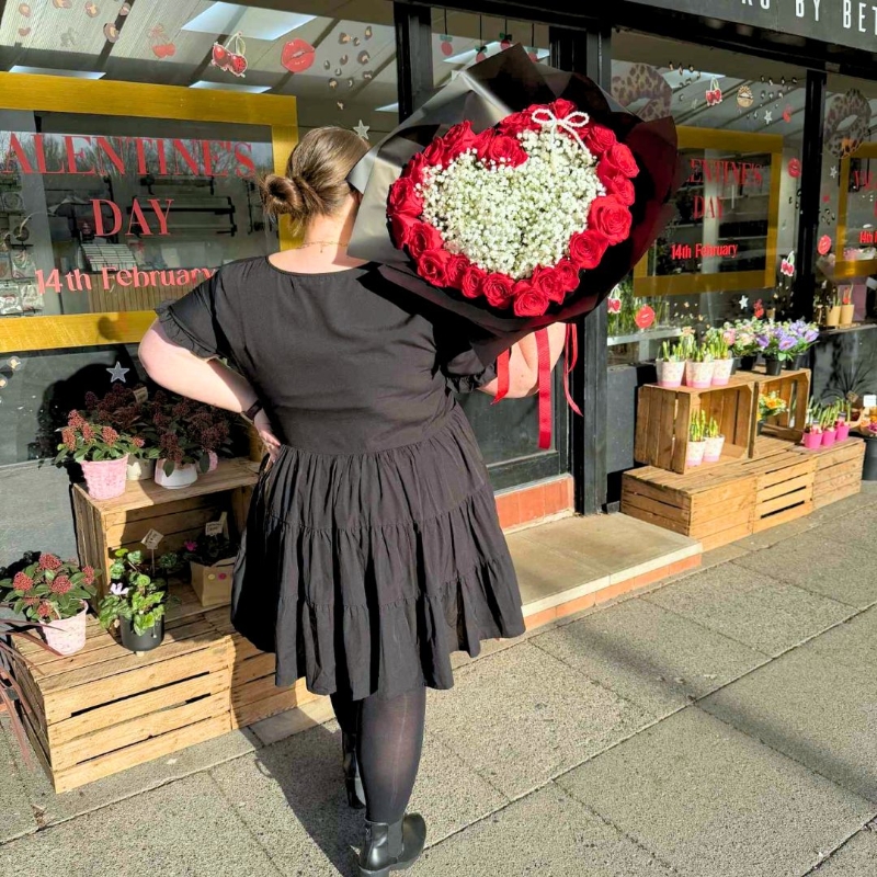 Valentine’s bouquet made with 24 premium red roses arranged around a white gypsophila heart with a pearl bow, wrapped in black with red ribbon, designed out of water with options for a gift bag with water bubble or upgrade to a modern glass vase.