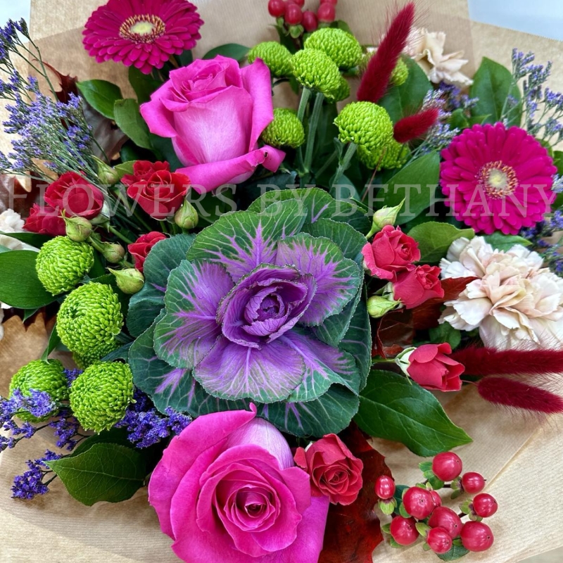 Autumn Jewel bouquet with fuchsia roses, gerbera, green chrysanthemums, berries and ornamental cabbage in kraft wrap.