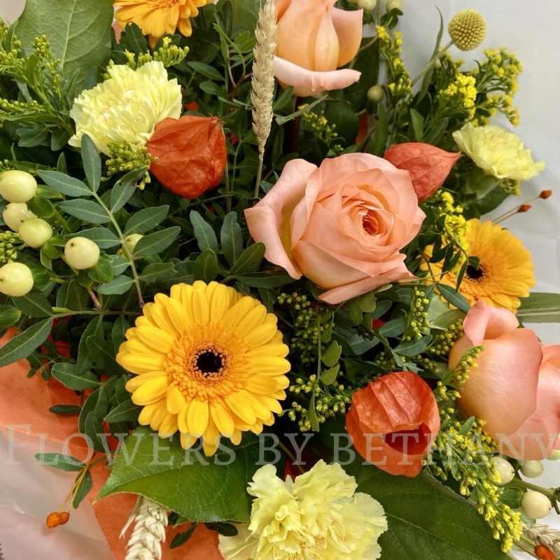 Honeycomb bouquet with peach roses, yellow carnations, gerbera and autumn foliage in orange gift wrap.
