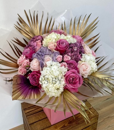 Luxury bouquet of roses, spray roses and hydrangea with gold leaf and ombré palm, presented in a pink gift bag.