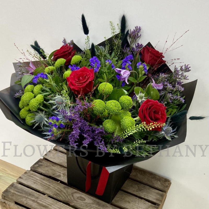 Elena bouquet with red roses, lime green blooms, purple flowers and thistle blue, hand-tied in black wrap.