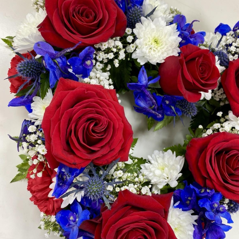 Mixed floral funeral heart tribute in red, white, and blue with luxury flowers representing British colours.