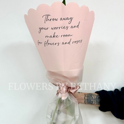 Hand-tied pink bouquet with seasonal florist’s choice florals and greenery, wrapped in scalloped blush pink paper with a satin ribbon.