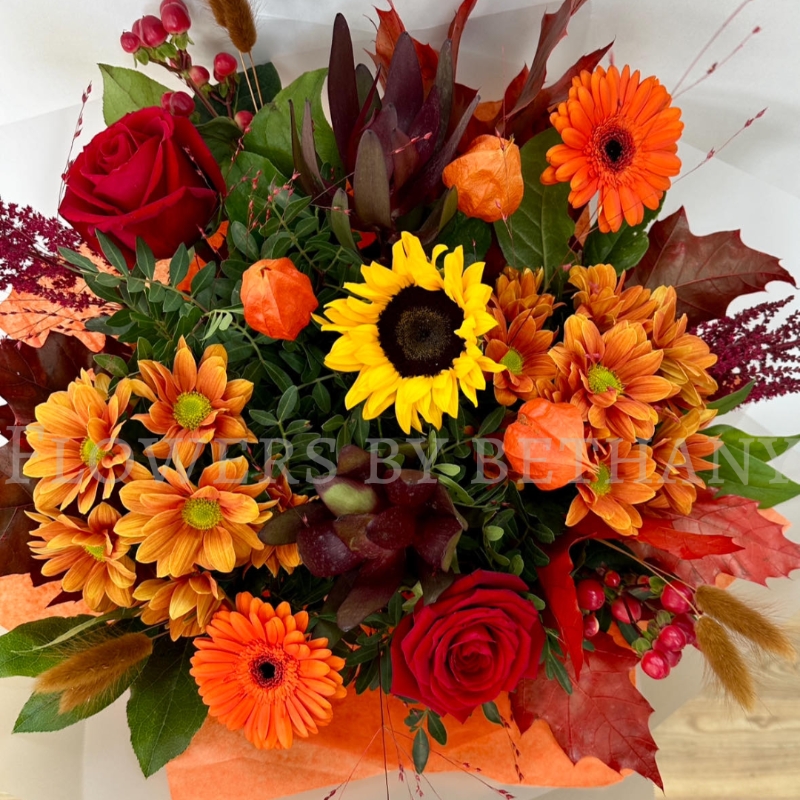 Pumpkin Spice bouquet with sunflower, orange gerbera, red roses, chrysanthemums and autumn foliage in gift wrap.