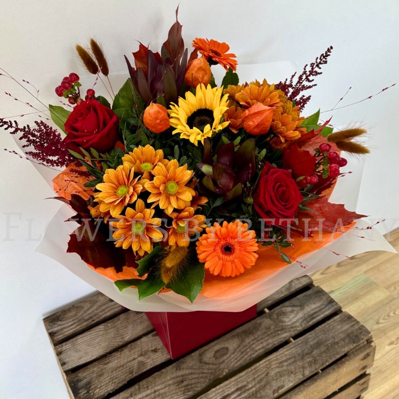 Pumpkin Spice bouquet with sunflower, orange gerbera, red roses, chrysanthemums and autumn foliage in gift wrap.