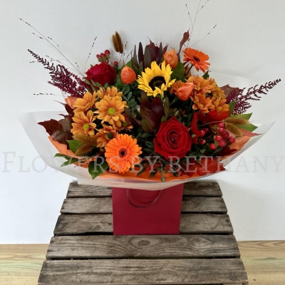 Pumpkin Spice bouquet with sunflower, orange gerbera, red roses, chrysanthemums and autumn foliage in gift wrap.
