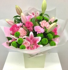 Hand-tied bouquet of pink lilies, pink roses, pink germini and lime chrysanthemums with mixed foliage in a gift bag.