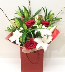 Hand-tied bouquet with red Freedom roses, white lilies, willow accents and foliage, wrapped in luxury cellophane and gift bag.