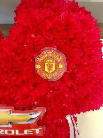 Manchester United shirt funeral tribute with fresh flower base, pipework detailing and printed waterproof badges, 21 x 21 inches, available in classic and modern shirt versions.