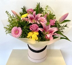 Pink and yellow seasonal florist’s choice hatbox arrangement with mixed florals and greenery.