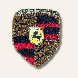 Porsche badge-shaped funeral tribute made with sprayed chrysanthemum in gold, red and black, finished with printed emblem and pipe cleaner accents.