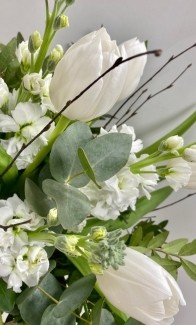 White Christmas vase arrangement with tulips, scented stocks, birch, mixed foliage and natural bow in a clear glass vase.