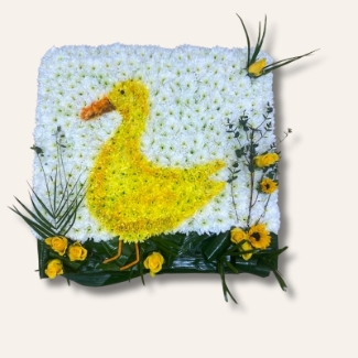 Duck-shaped funeral tribute made with white chrysanthemum, detailed with spray-painted shading and finished with foliage and yellow floral accents on a 2ft x 2ft base.