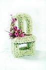 3D vacant chair-shaped funeral tribute made with white chrysanthemum and a soft pink floral focal on the seat, measuring approximately 57cm high, 28cm wide, and 21cm deep.
