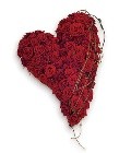 Contemporary swinging heart-shaped funeral tribute with massed red roses, bear grass, and natural foliage.