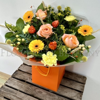 Honeycomb bouquet with peach roses, yellow carnations, gerbera and autumn foliage in orange gift wrap.
