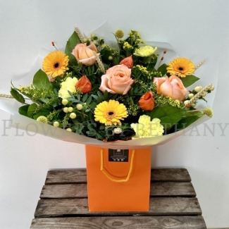 Honeycomb bouquet with peach roses, yellow carnations, gerbera and autumn foliage in orange gift wrap.