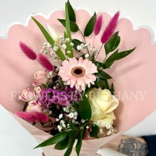 Hand-tied pink bouquet with seasonal florist’s choice florals and greenery, wrapped in scalloped blush pink paper with a satin ribbon.