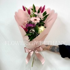 Hand-tied pink bouquet with seasonal florist’s choice florals and greenery, wrapped in scalloped blush pink paper with a satin ribbon.