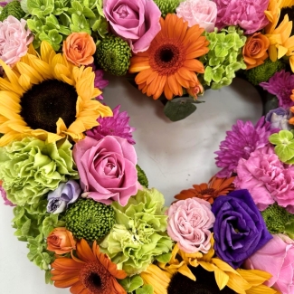 Heart-shaped funeral tribute featuring luxury summer-toned flowers in a vibrant mixed floral arrangement.