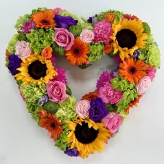 Heart-shaped funeral tribute featuring luxury summer-toned flowers in a vibrant mixed floral arrangement.