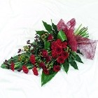 Deep red seasonal floral funeral spray with foliage, wrapped in luxury cellophane and a bow.
